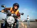 Uśmiechnięta kursantka na motorze, w kasku i kamizelce, uczy się jeździć. Zastanawiasz się, ile kosztuje prawo jazdy na motor?