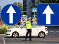 Policjant kieruje ruchem przy znakach droga jednokierunkowa. Biała Skoda czeka na sygnał.