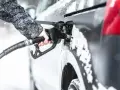 Ręka w zimowej kurtce trzyma pistolet do tankowania, nalewając diesel paliwo do samochodu podczas opadów śniegu.