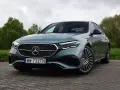 Elegancki Mercedes E220d w kolorze miętowym, zaparkowany na brukowanej nawierzchni, z zielenią w tle.