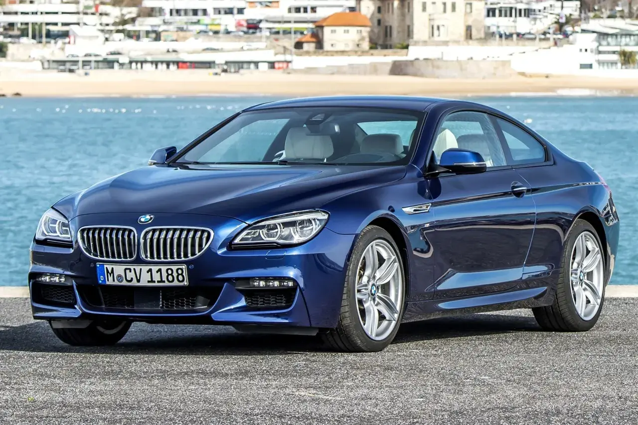 Granatowe BMW 640d coupe z jasnym wnętrzem zaparkowane nad błękitnym morzem, w tle zabudowania nadbrzeżne.