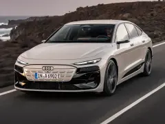 Jasnoszary Audi A6 e-tron jedzie po drodze z widokiem na ocean i góry.