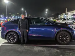 Mężczyzna stoi obok ciemnoniebieskiego Tesli Model Y na nocnym parkingu.