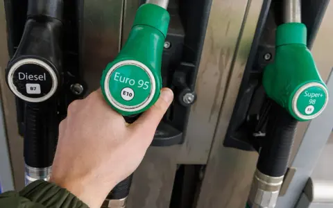Dłoń trzymająca zielony pistolet z napisem "Euro 95 E10" przy dystrybutorze paliwa. Idealny wybór dla silnika 1.3 multijet.