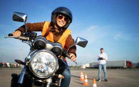 Uśmiechnięta kursantka na motorze, w kasku i kamizelce, uczy się jeździć. Zastanawiasz się, ile kosztuje prawo jazdy na motor?