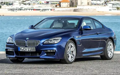 Granatowe BMW 640d coupe z jasnym wnętrzem zaparkowane nad błękitnym morzem, w tle zabudowania nadbrzeżne.