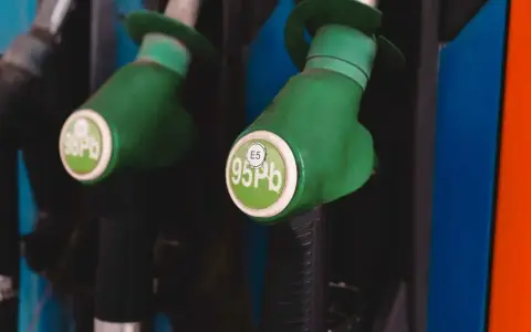 Dwa zielone pistolety dystrybutorów paliwa, jeden z napisem "98 Pb", drugi z "E5 95 Pb". Idealne do tankowania VW Polo 1.2 benzyna.