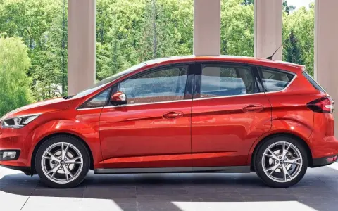 Czerwony Ford C-Max 1.6 benzyna zaparkowany pod arkadami, z zielenią w tle.
