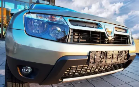 Złoty Dacia Duster 1.6 benzyna z chromowanym grillem i niebieskimi reflektorami, gotowy na przygodę pod błękitnym niebem.