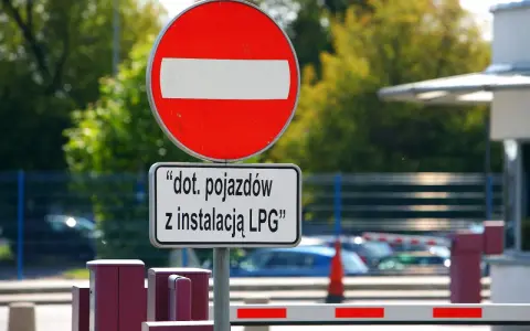 Znak B2 "zakaz wjazdu" z tabliczką informującą, że dotyczy pojazdów z instalacją LPG. Za znakiem widać szlaban i samochody.