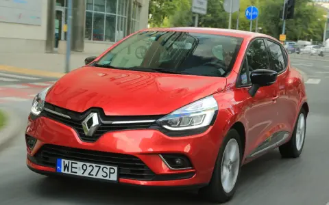 Czerwony Renault Clio 3 1.2 benzyna w ruchu miejskim. Kierowca w okularach przeciwsłonecznych.