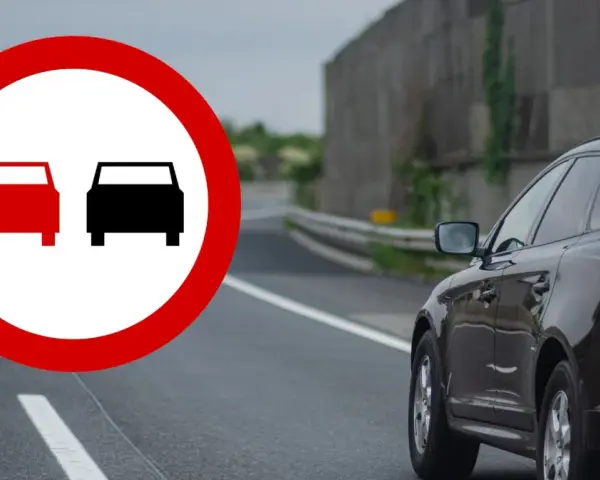 Znak zakazu wyprzedzania na drodze. Czarny SUV jedzie po prawej stronie, a z lewej widać znak z dwoma samochodami.