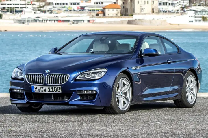 Granatowe BMW 640d coupe z jasnym wnętrzem zaparkowane nad błękitnym morzem, w tle zabudowania nadbrzeżne.