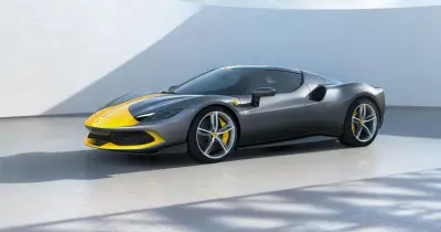 Szary Ferrari 296 GTB z żółtymi pasami na masce i dachu, stojący na betonowej posadzce.