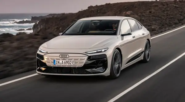 Jasnoszary Audi A6 e-tron jedzie po drodze z widokiem na ocean i góry.