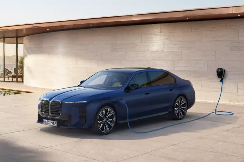 Elegancka, granatowa BMW hybryda podłączona do ładowarki przy nowoczesnym domu z widokiem na morze.